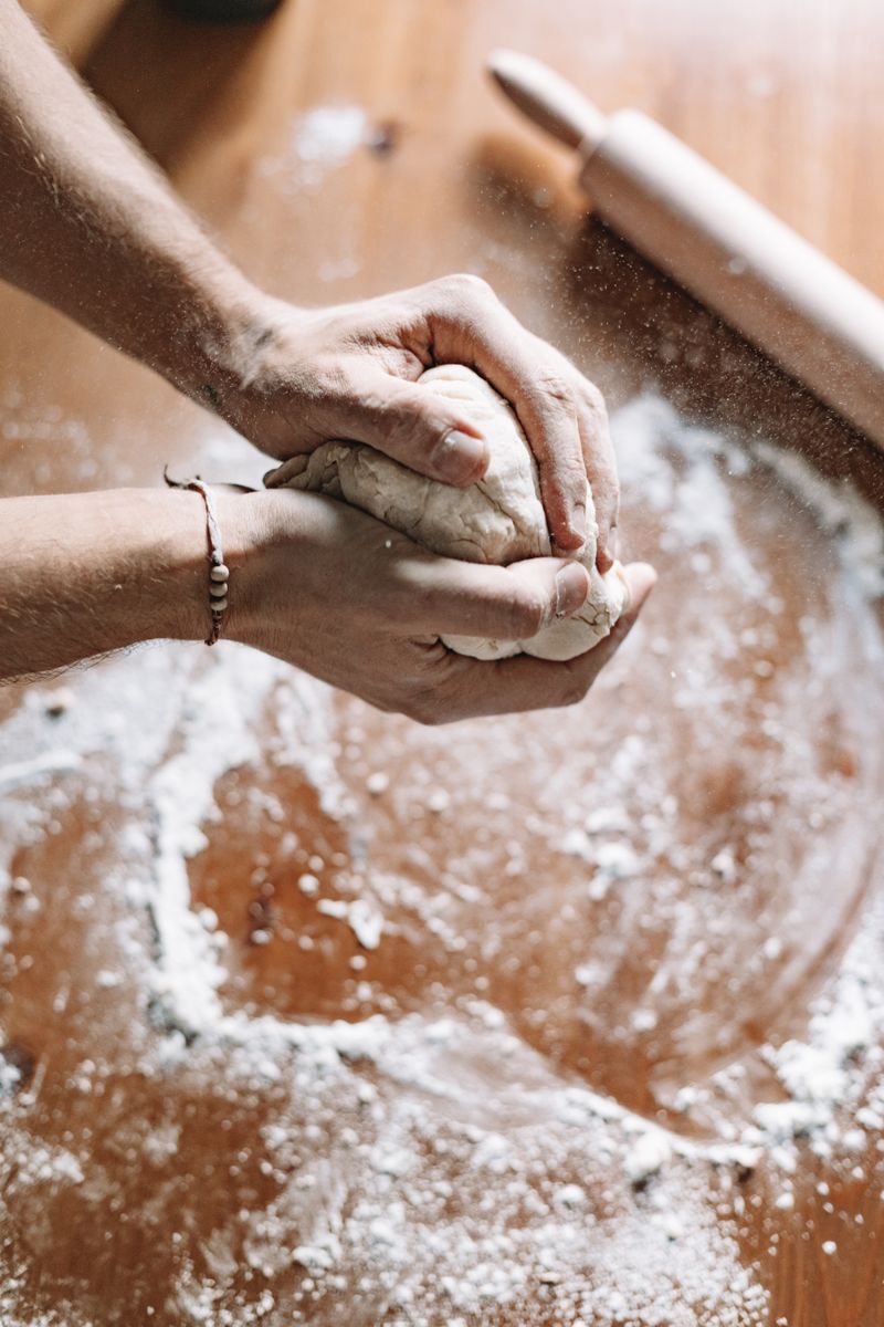 A baker's floured hands kneading dough on a wooden surface